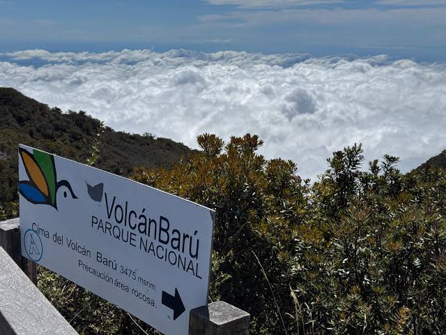 The Volcan Baru National Park sign at the summit, above a bank of clouds
